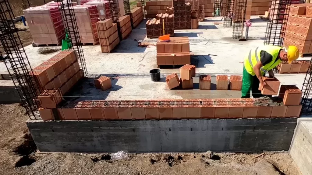 Muncitor așază un bloc ceramic pe patul de mortar