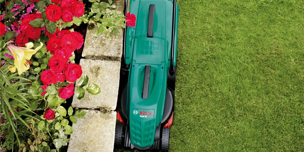 Mașină Bosch pentru tuns gazonul lângă marginea unei alei cu flori